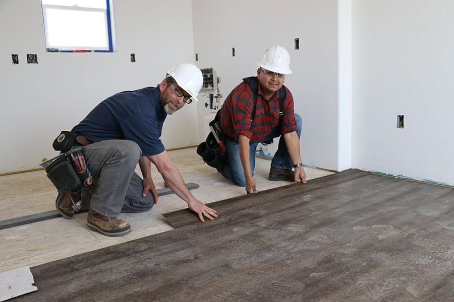 A San Juan College student with a professor laying flooring in a house.